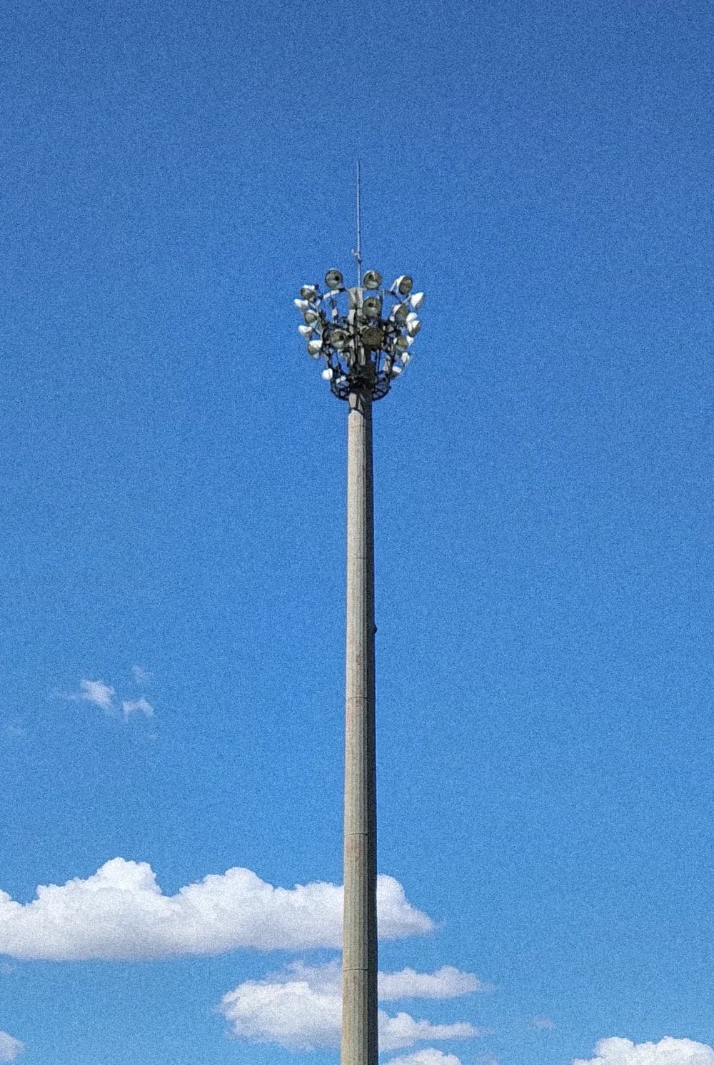 A tall concrete floodlight pole crowned with lamps, against a deep blue sky with a few clouds low in the frame.