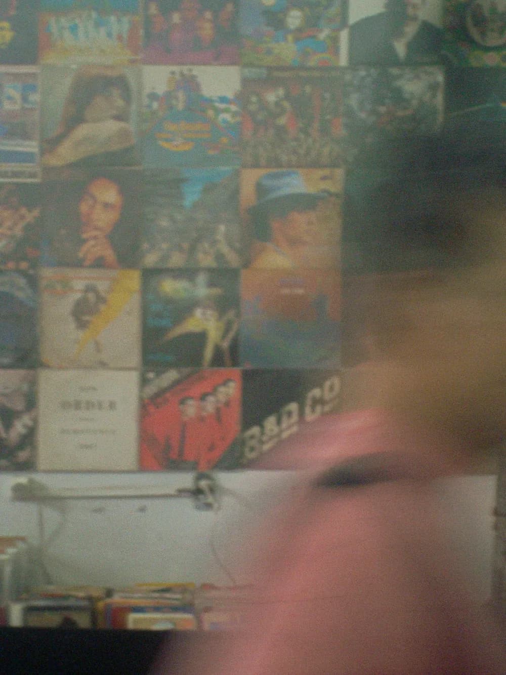 A wall of album covers behind a face moving too fast for the shutter, all soft and grainy.