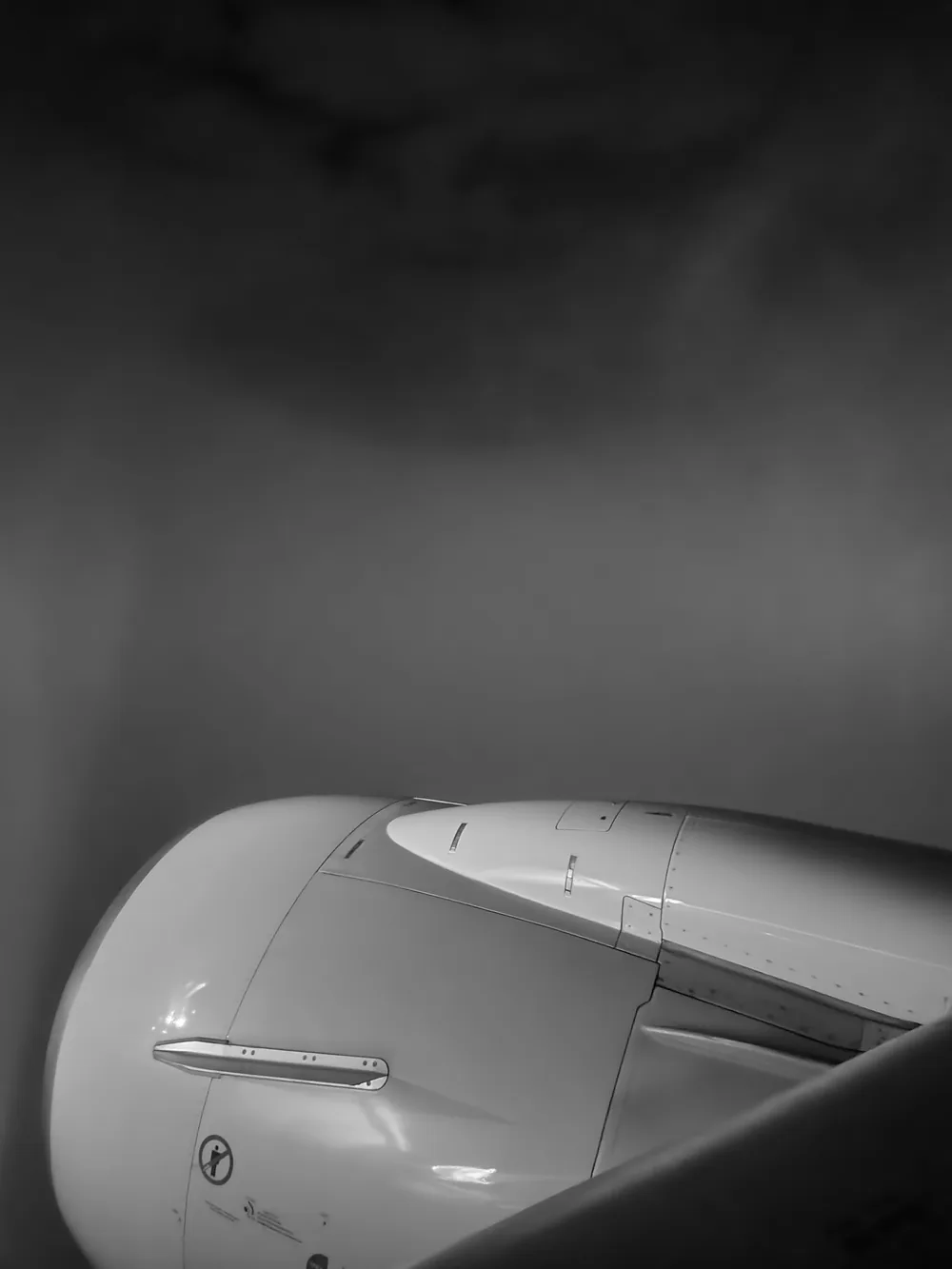 Black and white close view of an aeroplane engine cowling under a dark, cloudy sky.